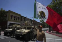 Un manifestante ondea una bandera de México junto a elementos de la Guardia Nacional de California estacionada en una calle de Santa Ana, California, el martes 10 de junio de 2025. (AP Foto/Jae C. Hong)