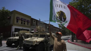 Un manifestante ondea una bandera de México junto a elementos de la Guardia Nacional de California estacionada en una calle de Santa Ana, California, el martes 10 de junio de 2025. (AP Foto/Jae C. Hong)