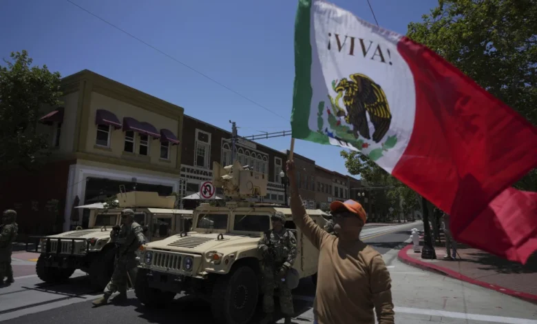 Un manifestante ondea una bandera de México junto a elementos de la Guardia Nacional de California estacionada en una calle de Santa Ana, California, el martes 10 de junio de 2025. (AP Foto/Jae C. Hong)