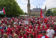 Decenas de miles de personas vestidas de rojo marchan frente al Palacio de la Paz, sede de la Corte Internacional de Justicia, al fondo, para exigir que su gobierno haga más para frenar la campaña militar de Israel en la Franja de Gaza, el domingo 15 de junio de 2025, en La Haya, Holanda. (AP Foto/Peter Dejong)
