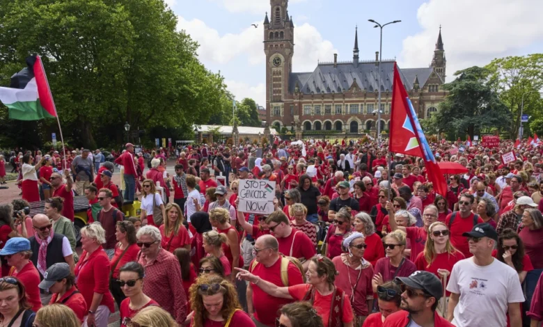 Decenas de miles de personas vestidas de rojo marchan frente al Palacio de la Paz, sede de la Corte Internacional de Justicia, al fondo, para exigir que su gobierno haga más para frenar la campaña militar de Israel en la Franja de Gaza, el domingo 15 de junio de 2025, en La Haya, Holanda. (AP Foto/Peter Dejong)
